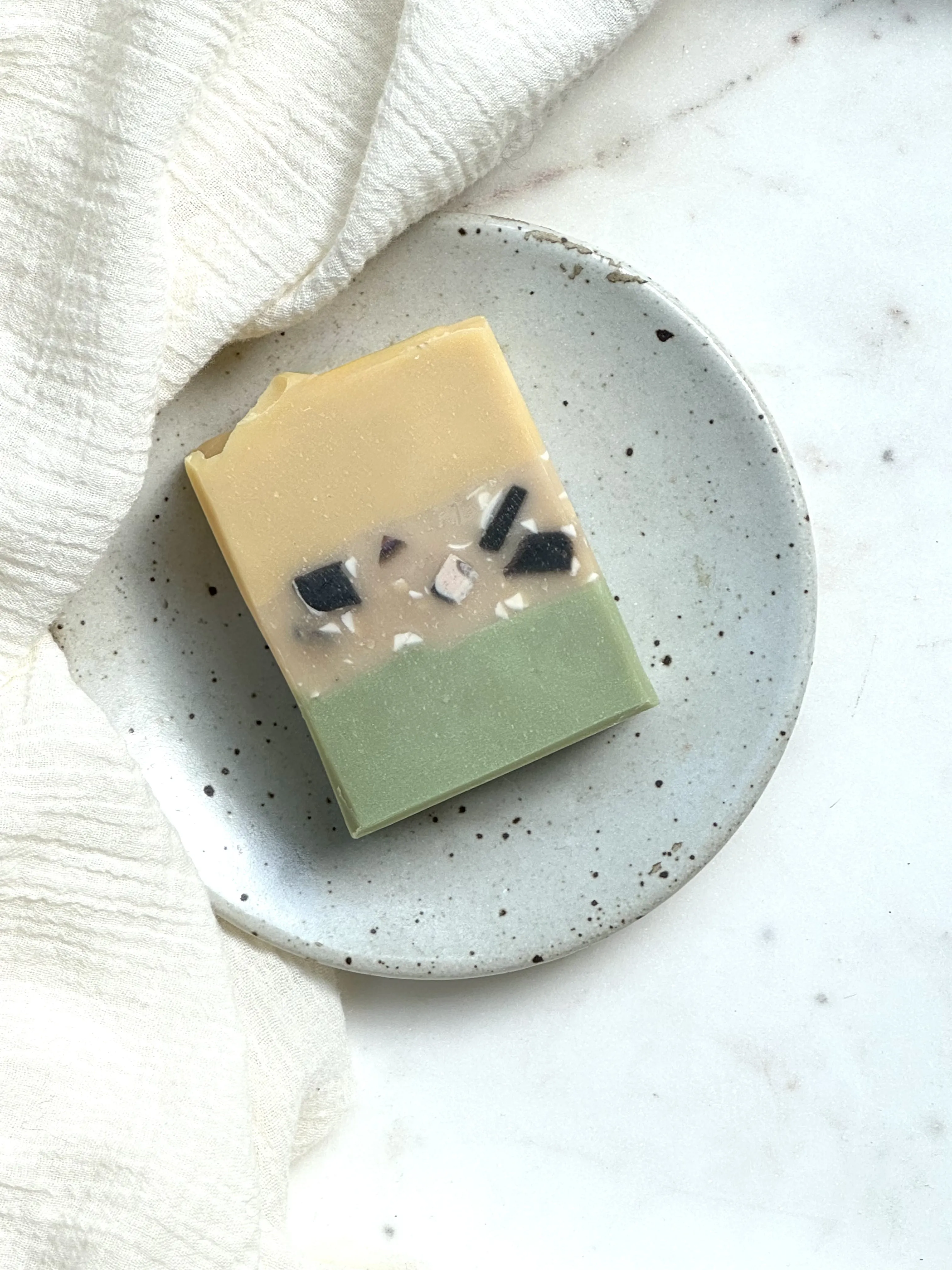 Bar soap laying on ceramic soap dish with cloth backdrop