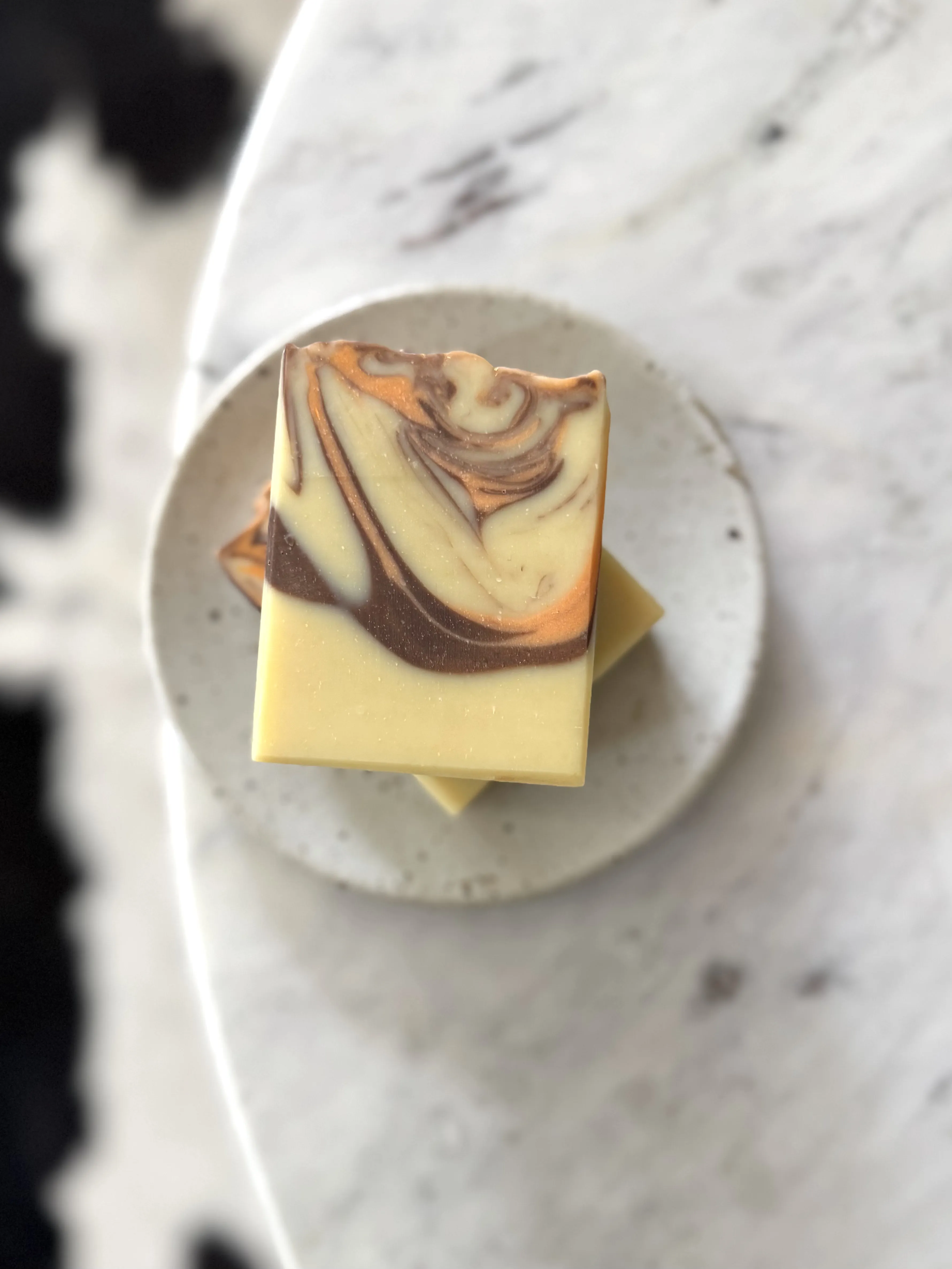 Bar soap with brown and orange swirl on a grey soap dish and white marble background